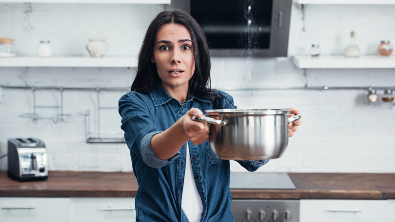 Amazed girl using steel pot during water leak in kitchen