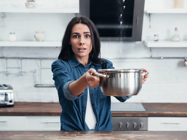 Amazed girl using steel pot during water leak in kitchen